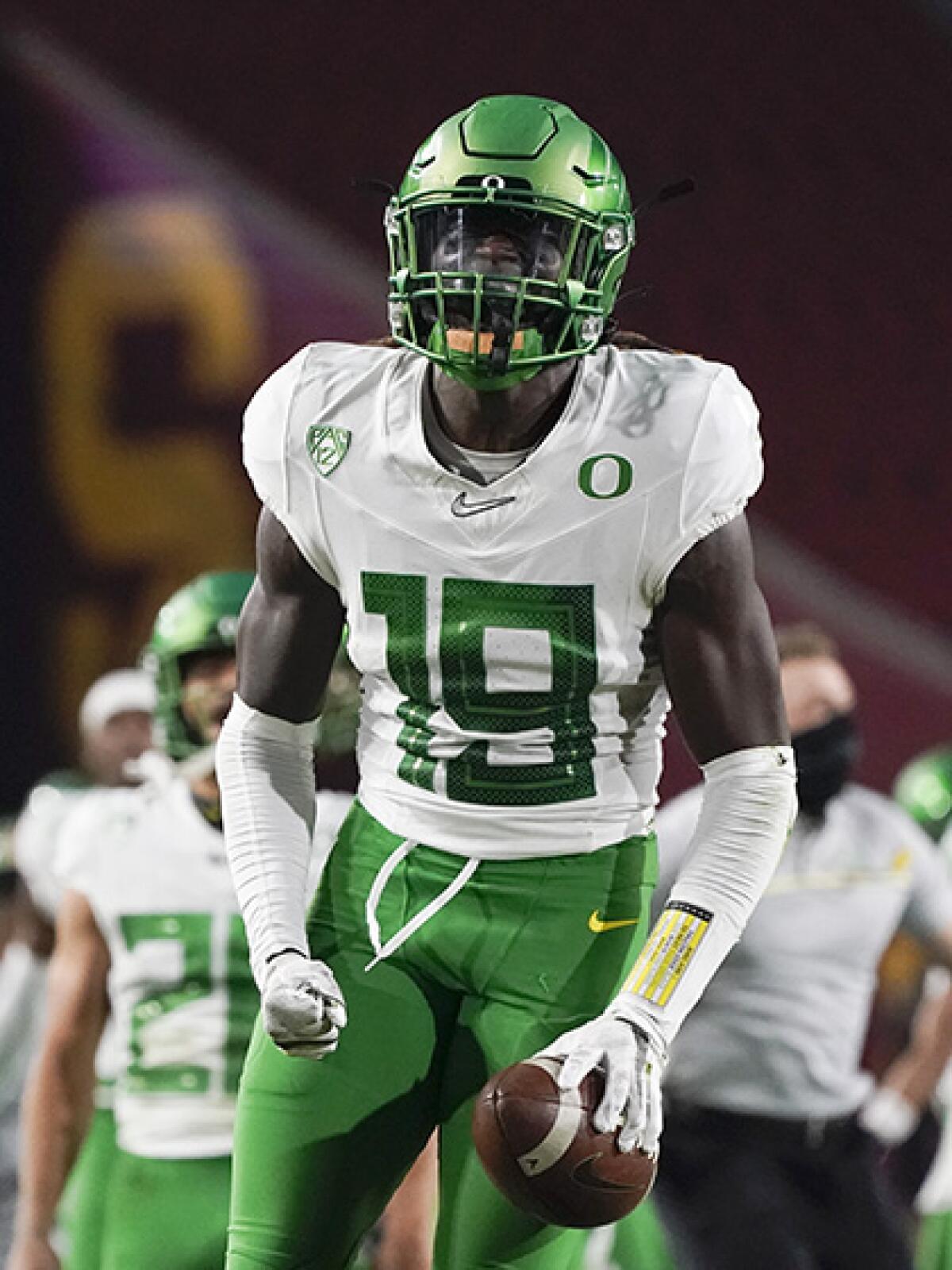 Oregon's Jamal Hill holds a football on the field with teammates behind him.