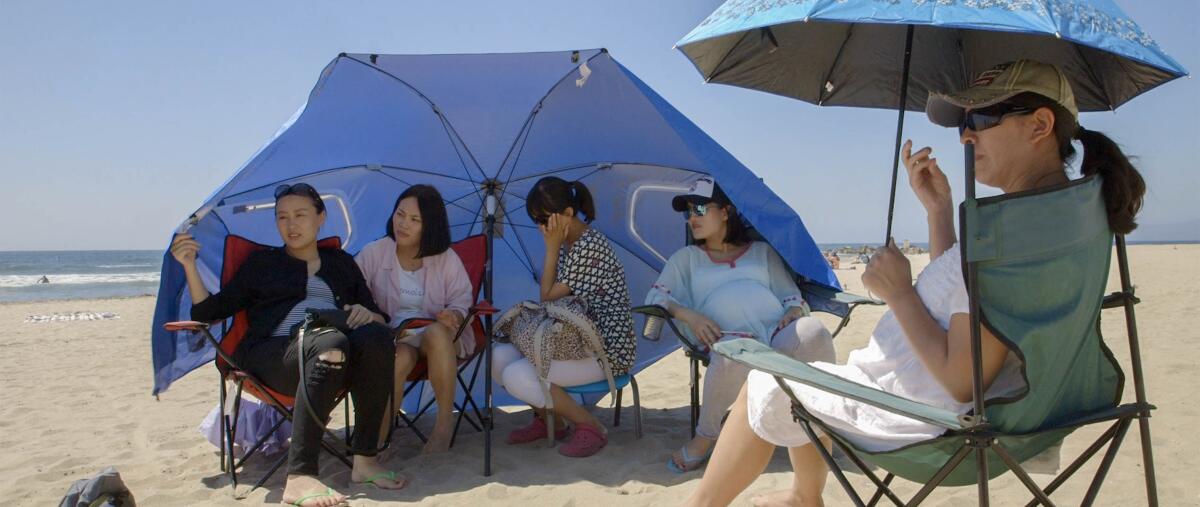 Several people sitting in chairs on the sand under beach umbrellas, the ocean in the background