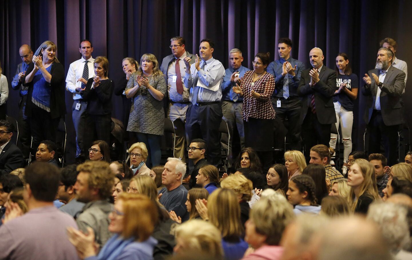 High school principals, Newport-Mesa Unified School District officials and other community members give a standing ovation to a Holocaust survivor who attended Monday night's discussion concerning pictures that emerged from a weekend party showing students saluting a swastika made of red plastic cups.
