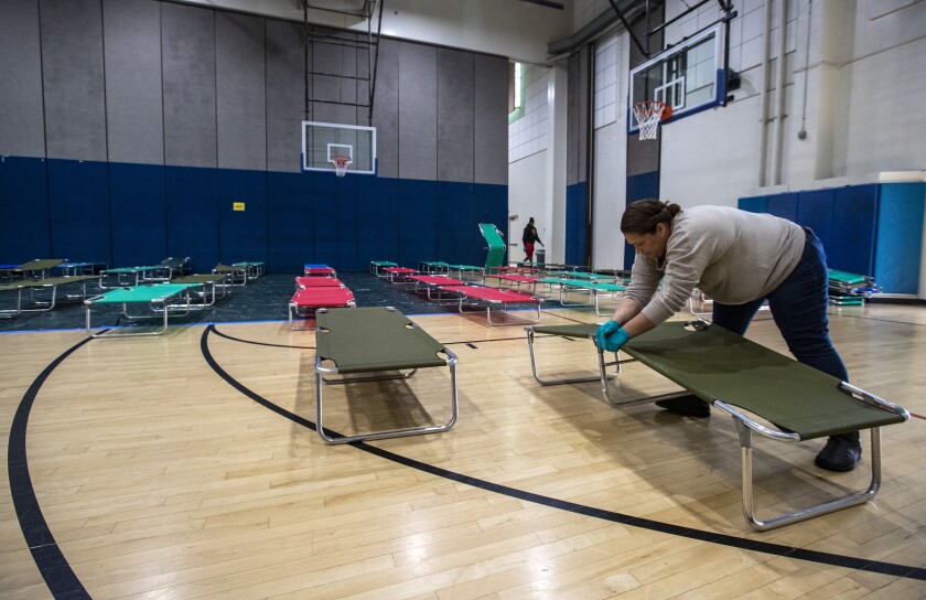 Why a fight over homeless people could determine how much coronavirus hurts California 4 Salvation Army volunteer Christina Cuevas sets up cots for homeless people at Westwood Recreation Center in Los Angeles.
