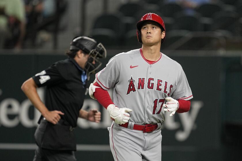 Los Angeles Angels' Shohei Ohtani jogs to the dugout past home plate umpire John Tumpane, rear, after Ohtani grounded out during the eighth inning of the team's baseball game against the Texas Rangers, Tuesday, Aug. 15, 2023, in Arlington, Texas. (AP Photo/Tony Gutierrez)