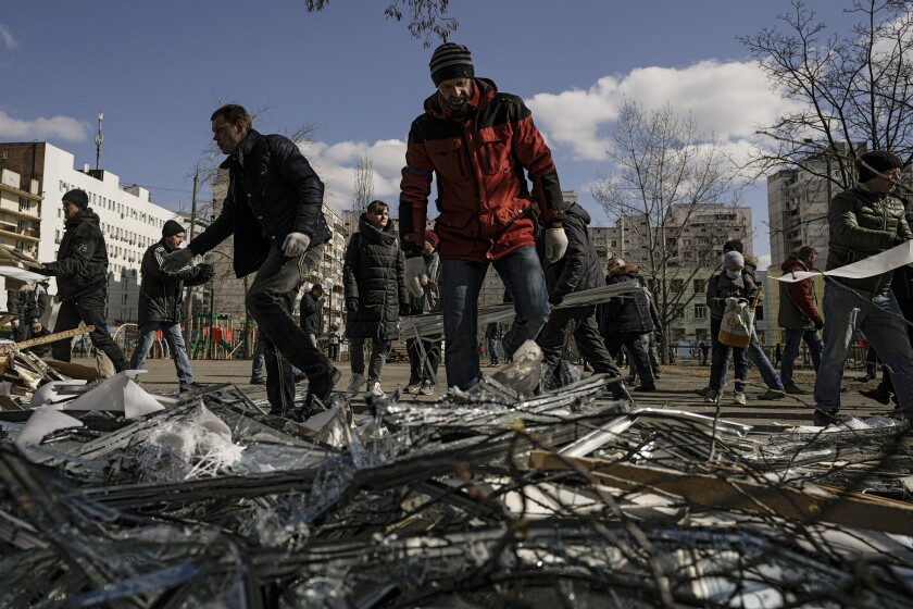 People clear debris outside a medical center damaged after parts of a Russian missile, shot down by Ukrainian air defense, landed on a nearby apartment block, according to authorities, in Kyiv, Ukraine, Thursday, March 17, 2022. Russian forces destroyed a theater in Mariupol where hundreds of people were sheltering Wednesday and rained fire on other cities, Ukrainian authorities said, even as the two sides projected optimism over efforts to negotiate an end to the fighting. (AP Photo/Vadim Ghirda)