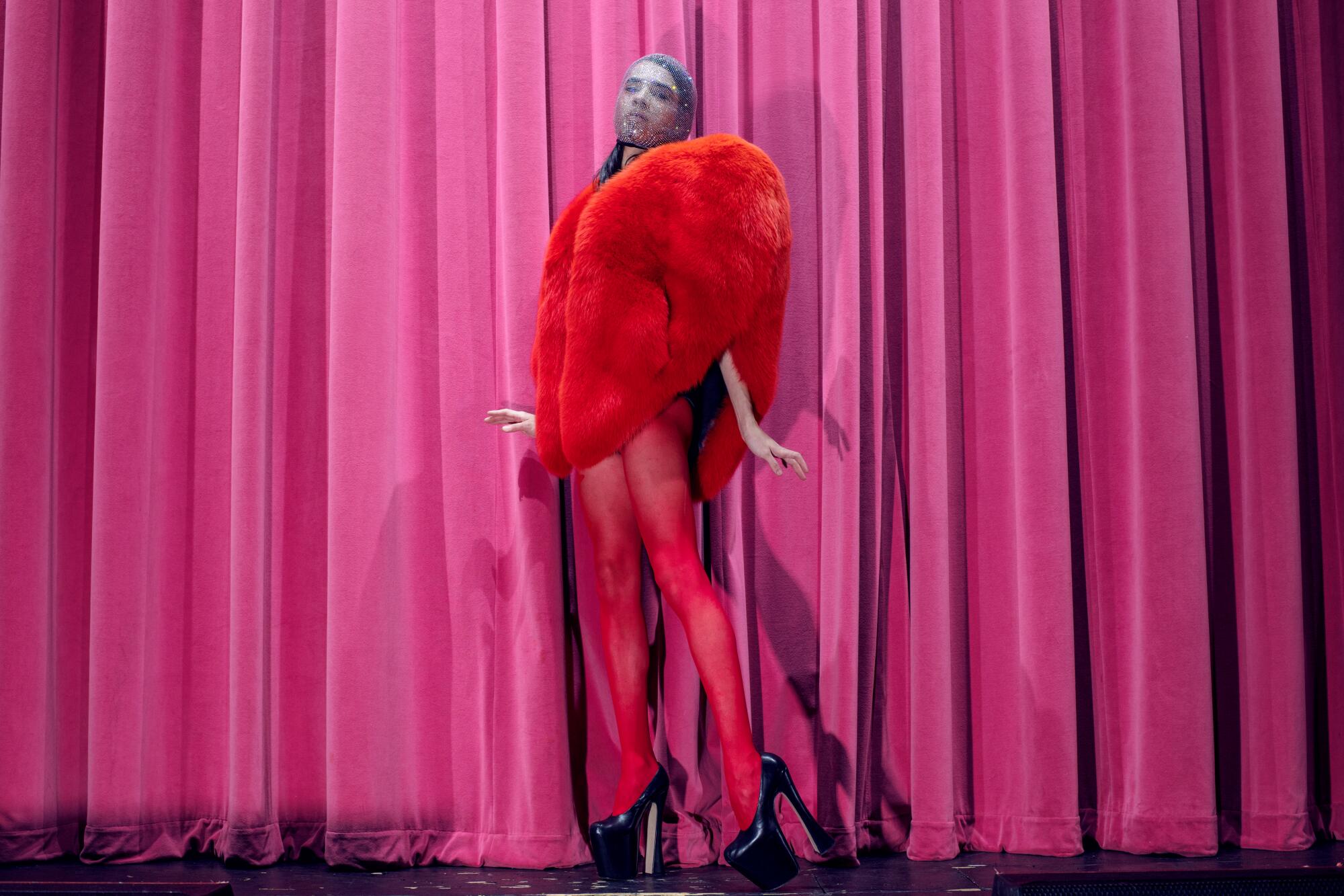 A woman in all red poses before a pink curtain.