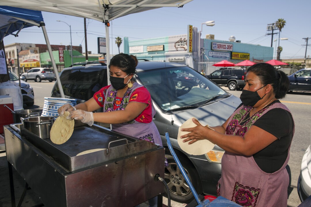 Two women make tortillas under a tent outside