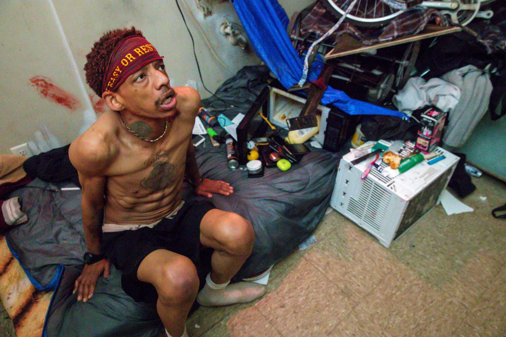 A man seated on a mattress in his hotel unit