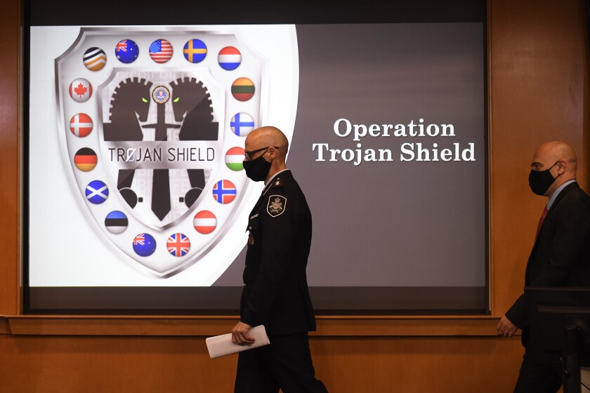 Law enforcement officials walk past an Operation Trojan Shield logo at a news conference, Tuesday, June 8, 2021, in San Diego. The global sting operation involved an encrypted communications platform developed by the FBI and has sparked a series of raids and arrests around the world in which more than 800 suspects were arrested and more than 32 tons of drugs — cocaine, cannabis, amphetamines and methamphetamines were seized. (AP Photo/Denis Poroy)