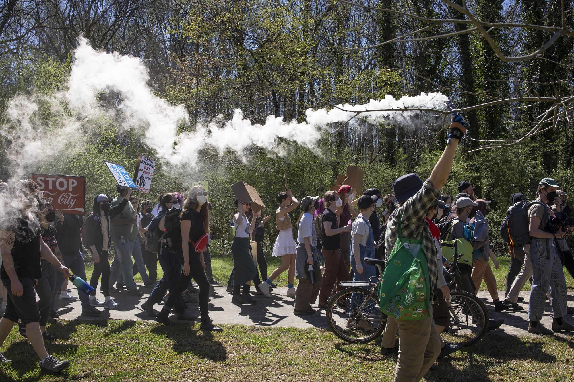 Activists demonstrate in a forest, one holding a smoking flare. 