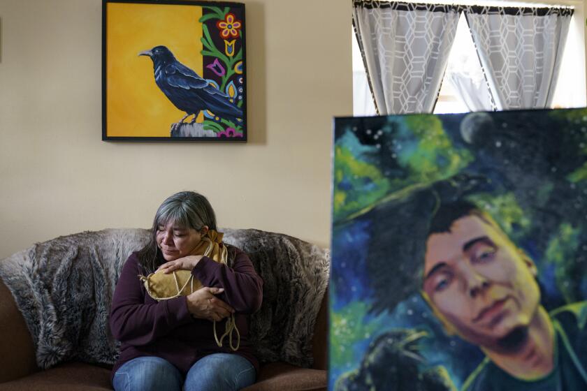 Rachel Taylor clutches a buckskin satchel filled with the ashes of her son, Kyle "Little Crow" Domrese, pictured at right, who died of an overdose, as she sits in the home they shared in Bemidji, Minn., Wednesday, Nov. 17, 2021. Just weeks remained until the anniversary of the day she opened his bedroom door and found her son face-down on his bed, one of more than 100,000 Americans lost in a year to overdoses as the COVID-19 pandemic aggravated America's addiction disaster. The death rate from drug overdoses for Native Americans has surpassed white people and is now the highest in the nation. (AP Photo/David Goldman)