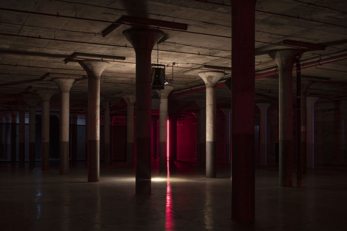 A single red neon light is visible at the center of a dim warehouse space