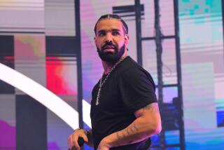 Man, drake, wearing black shirt and diamond chain, walking sideways with hands to side while performing on stage