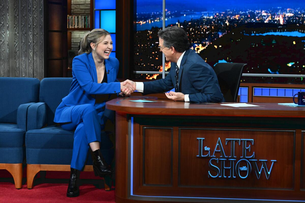 Taylor Tomlinson in a blue suit shakes Stephen Colbert's hand.