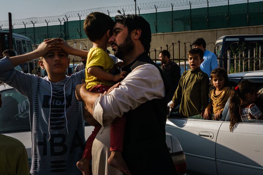 KABUL, AFGHANISTAN -- AUGUST 19, 2021: A father rests his head on his childOs face as his elder son puts both his hands on his head in despair on the road to the military entrance of the airport for evacuations, in Kabul, Afghanistan, Thursday, Aug. 19, 2021.Here Afghans are made to wait behind the first Taliban checkpoint, before bringing their worldly possessions one can only carry in both hands to the military gate for evacuations out of the country. A few hundred people congregate there listening to spotty announcements from a skinny Taliban fighter with neck-length hair standing on an elevated platform, wearing a surgical mask for covid19 prevention, but barely covering his mouth. On his right hand a cold water bottle. On his left hand a semi-automatic pistol and a walkie talkie radio that he occasionally waves to the crowd to get their attention. The Taliban fighter with the pistol announces that they will call out names of countries and people with approval for flights to those countries will be allowed to pass. (MARCUS YAM / LOS ANGELES TIMES)