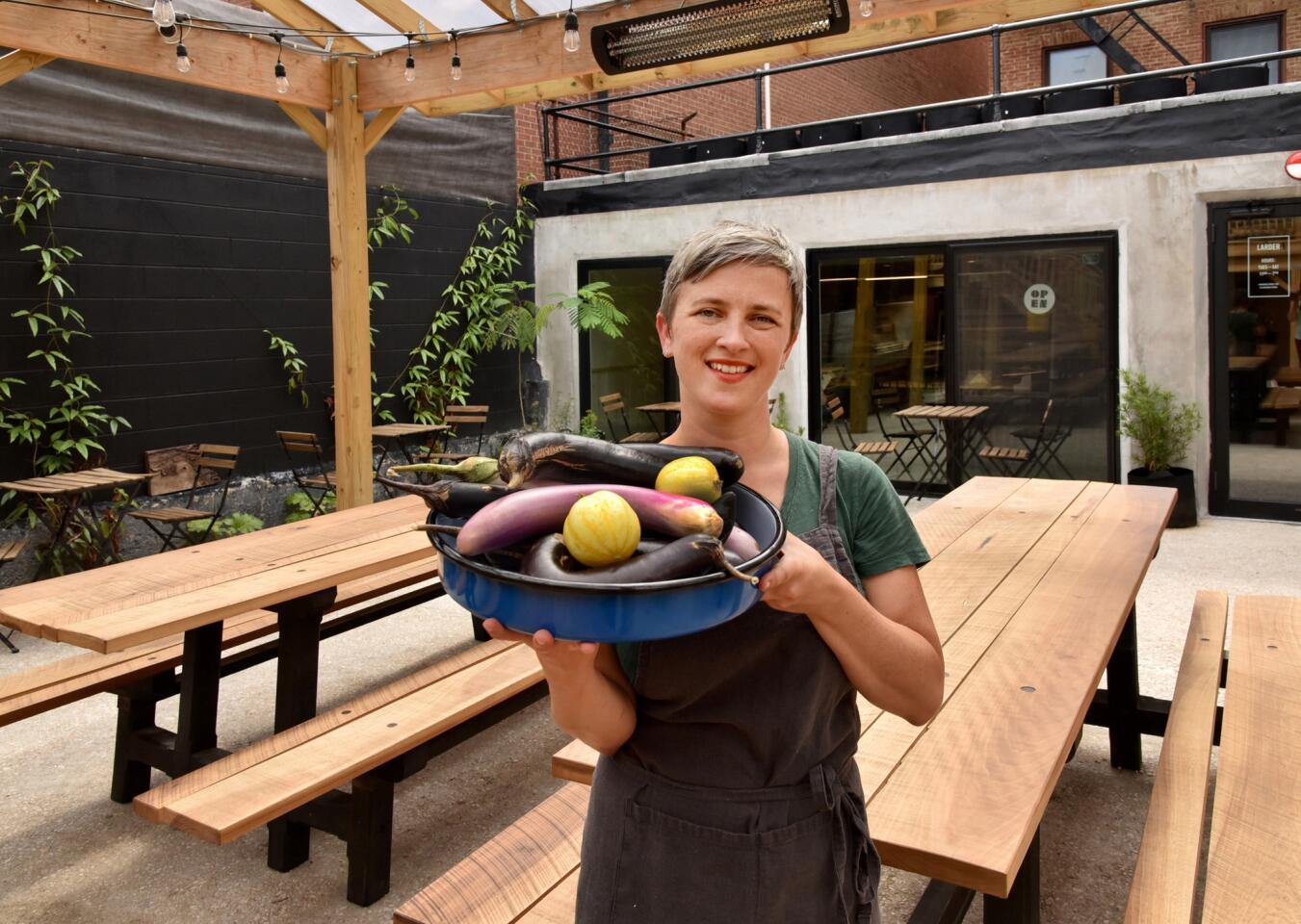 Chef-owner Helena del Pesco, holding a bounty of local vegetables, in the covered dining patio at Larder Baltimore, a farm-to-table restaurant.