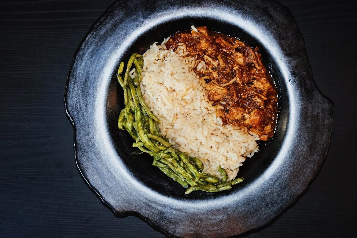 A bowl of food laid in three rows: green shredded cactus, white rice and red-brown pork belly in sauce on a black table
