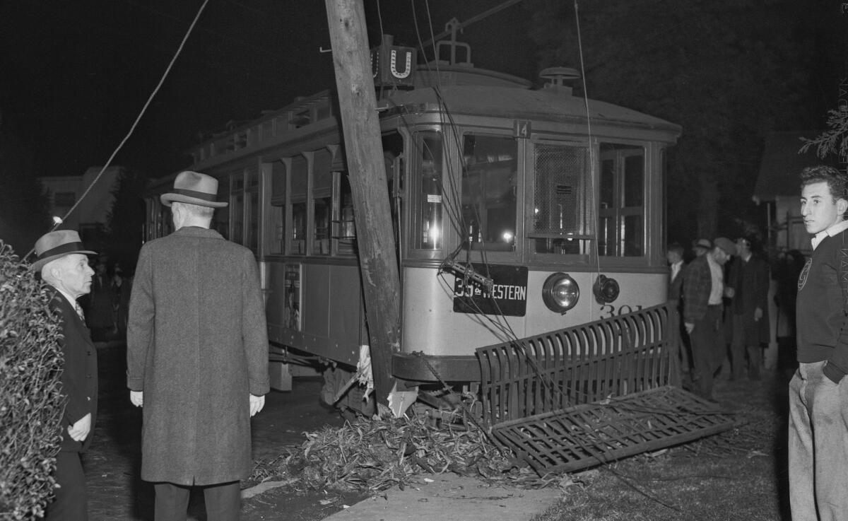 Men in hats stand near a street car that has smashed into a power pole.