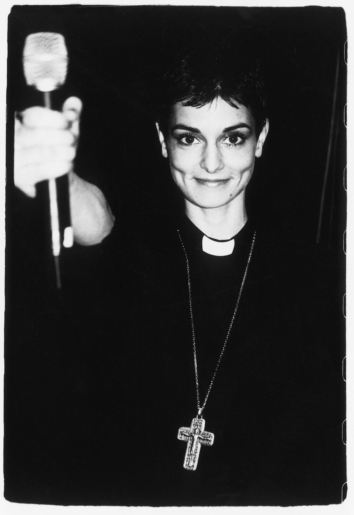A vintage photo of Sinéad O'Connor wearing a priest's collar and crucifix.