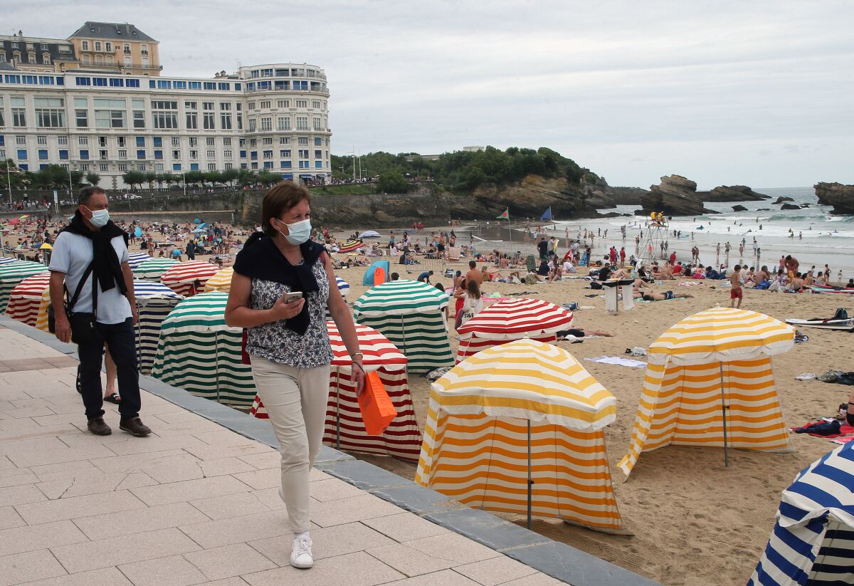 FILE - In this Wednesday, July 28, 2021 file photo, people wear face masks, to protect against coronavirus, walk on the pedestrian promenade along the beach in Biarritz, southwestern France. The majority of families with low income living in the European Union, the world's largest economy, can't afford a summer holiday, according to a study by the the European Trade Union Confederation (ETUC) released on Monday, Aug. 2, 2021. (AP Photo/Bob Edme, File)