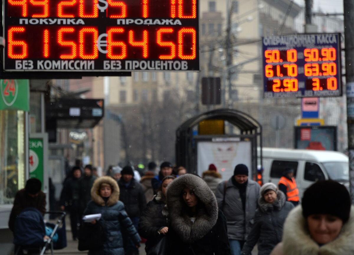 Pedestrians walk under a board listing foreign currency rates against the Russian ruble in central Moscow on Monday.