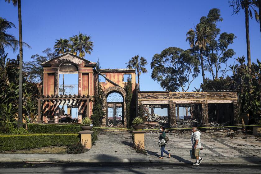 Laguna Niguel, CA - May 12: Venus Shafizadah, left, and her husband Ata Shafizadah, evacuated last evening, came to pick necessary medicines from their home escaped any fire damage. Shafizadahs walk by smoldering homes on their home street on Coronado Pointe on Thursday, May 12, 2022 in Laguna Niguel, CA. (Irfan Khan / Los Angeles Times)