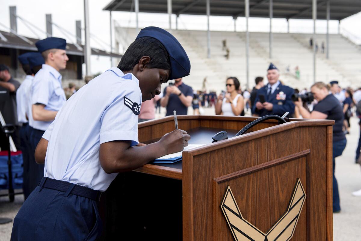 A woman in an Air Force uniform signs a document on a lectern. 