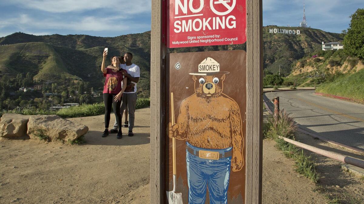 San Fernando Valley residents Kimani Larry, left, and John Flowers stop on Lake Canyon Drive for a selfie with the Hollywood sign in the background.