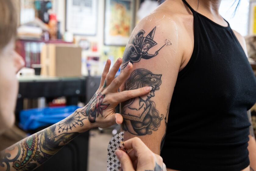 Encinitas, CA - October 17: Tattoo artist Lauren Bartram (left) wipes clean up her client Jasmine Lugo's (right) newest tattoo of one of the fairies from the movie Sleeping Beauty at the 454 Tattoo in Encinitas, CA on Monday, Oct. 17, 2022. (Adriana Heldiz / The San Diego Union-Tribune)