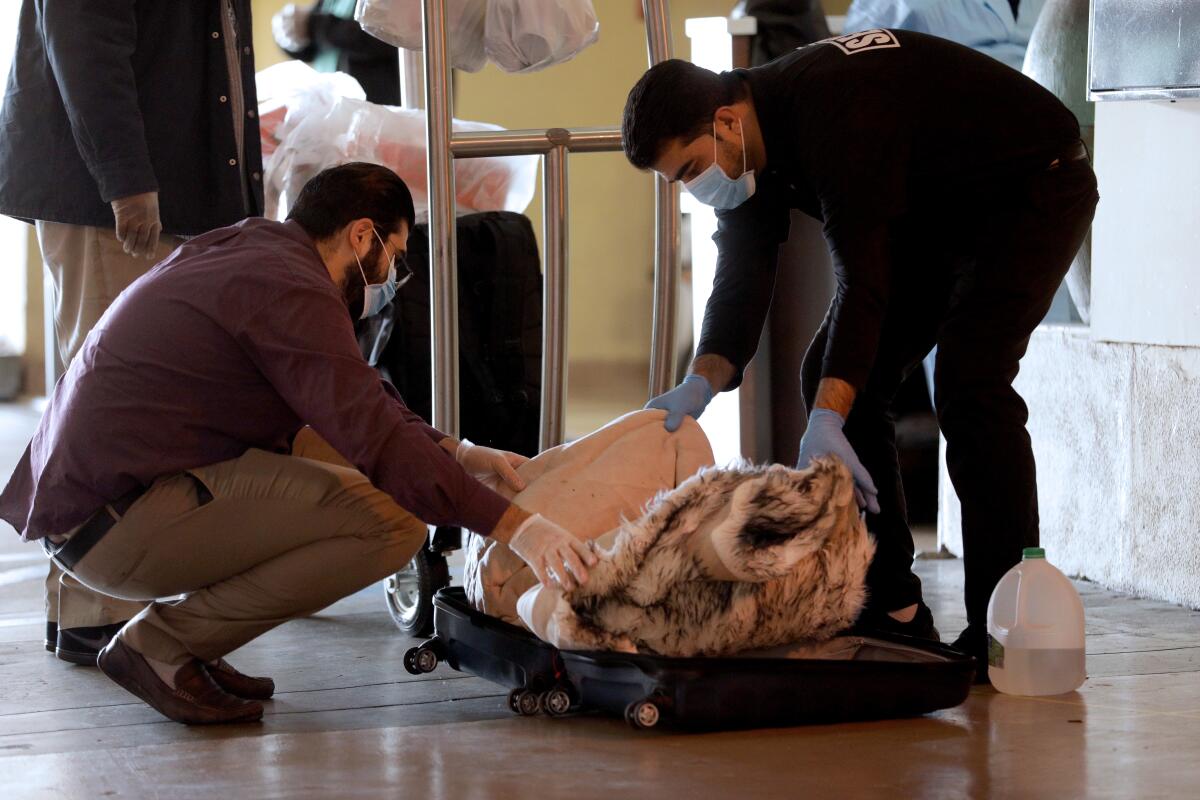 Two men wearing medical face masks look into a suitcase 