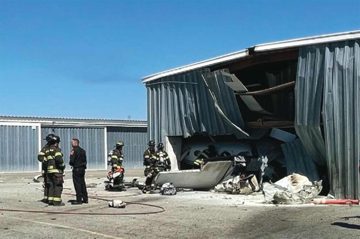 Firefighters stand next to a small plane crashed into the side of an aircraft hangar