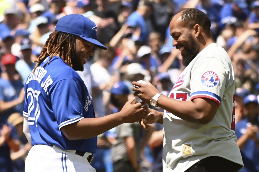 Toronto Blue Jays' Vladimir Guerrero, right, signs a baseball with his son, Vladimir Guerrero Jr., after throwing out the ceremonial first pitch prior to a baseball game against the Tampa Bay Rays, Saturday, July 2, 2022 in Toronto. (Jon Blacker/The Canadian Press via AP)