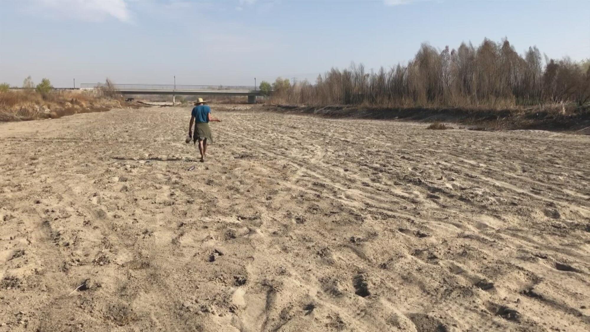 A man walks on a dry, sandy riverbed.