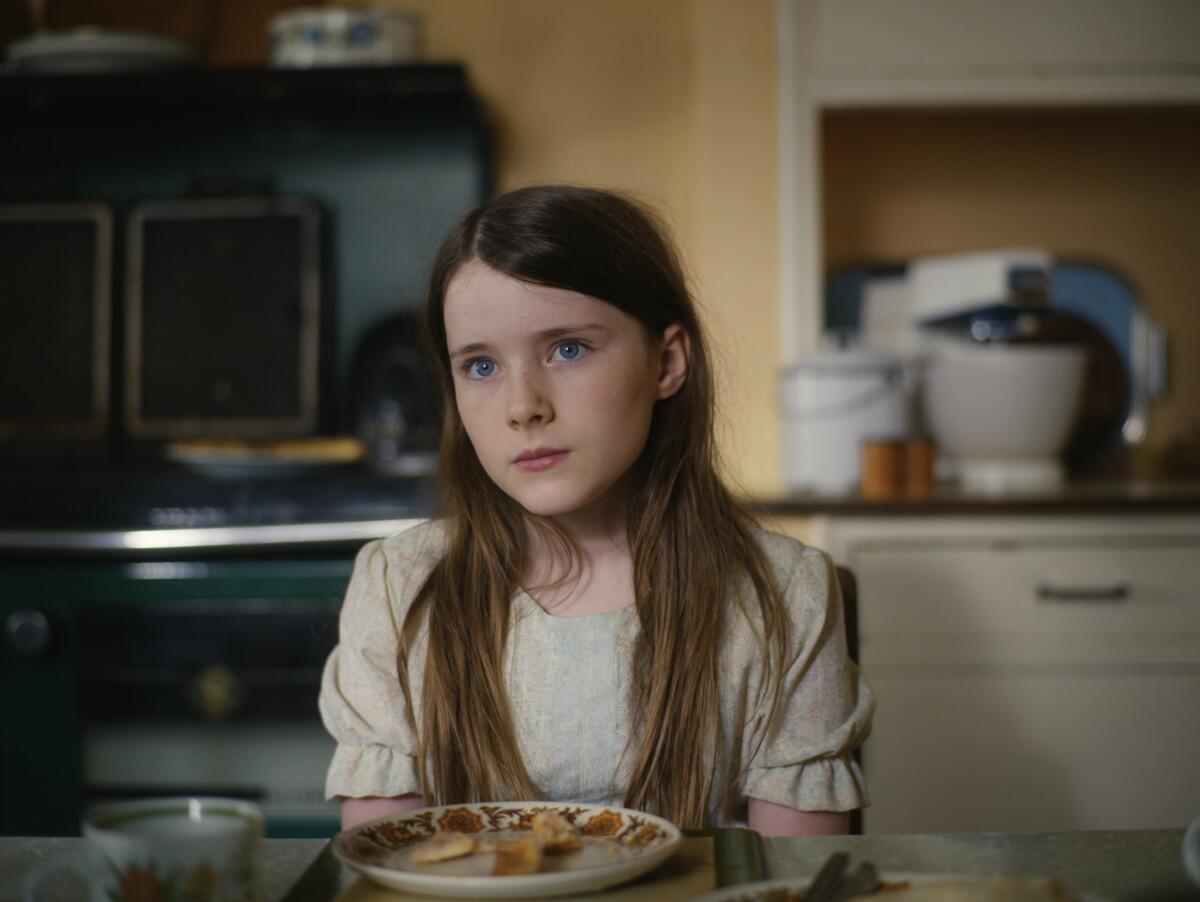 A girl with long brown hair sits at a kitchen table in a scene from 'The Quiet Girl'