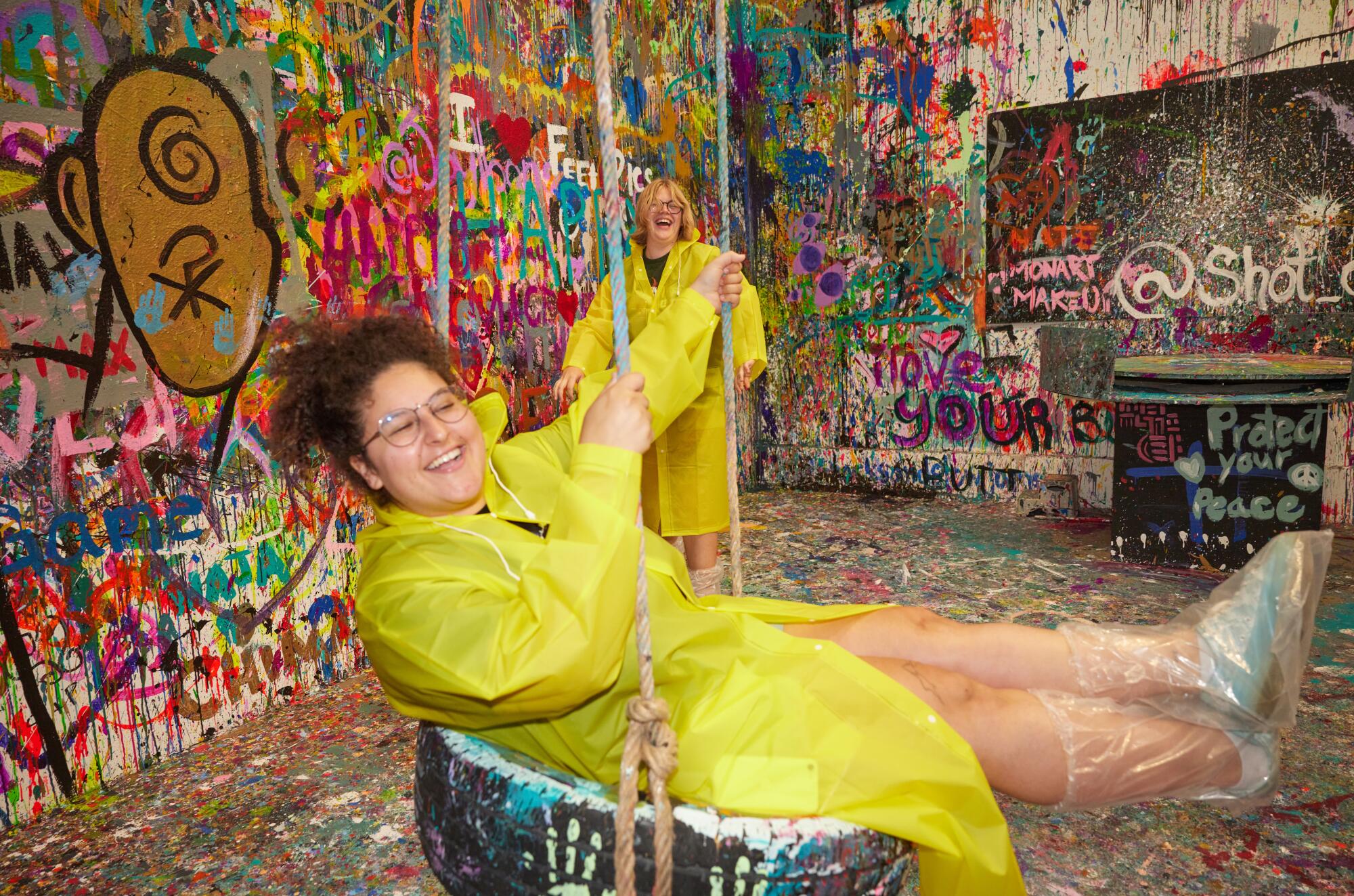 A person wearing a yellow raincoat smiles on a tire swing.