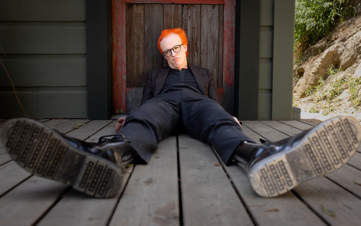 Man with bright orange hair laying on the ground, boots up