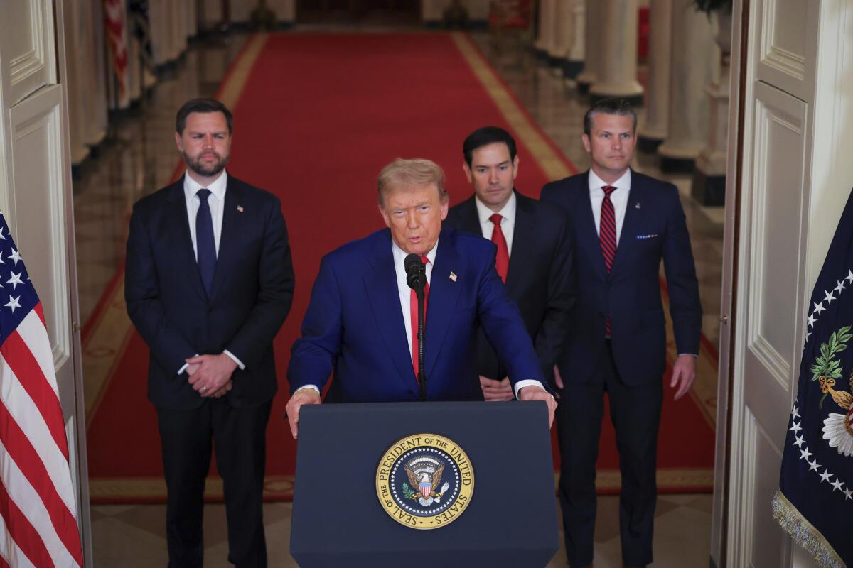 Four men stand at a lectern, in front of a red carpet