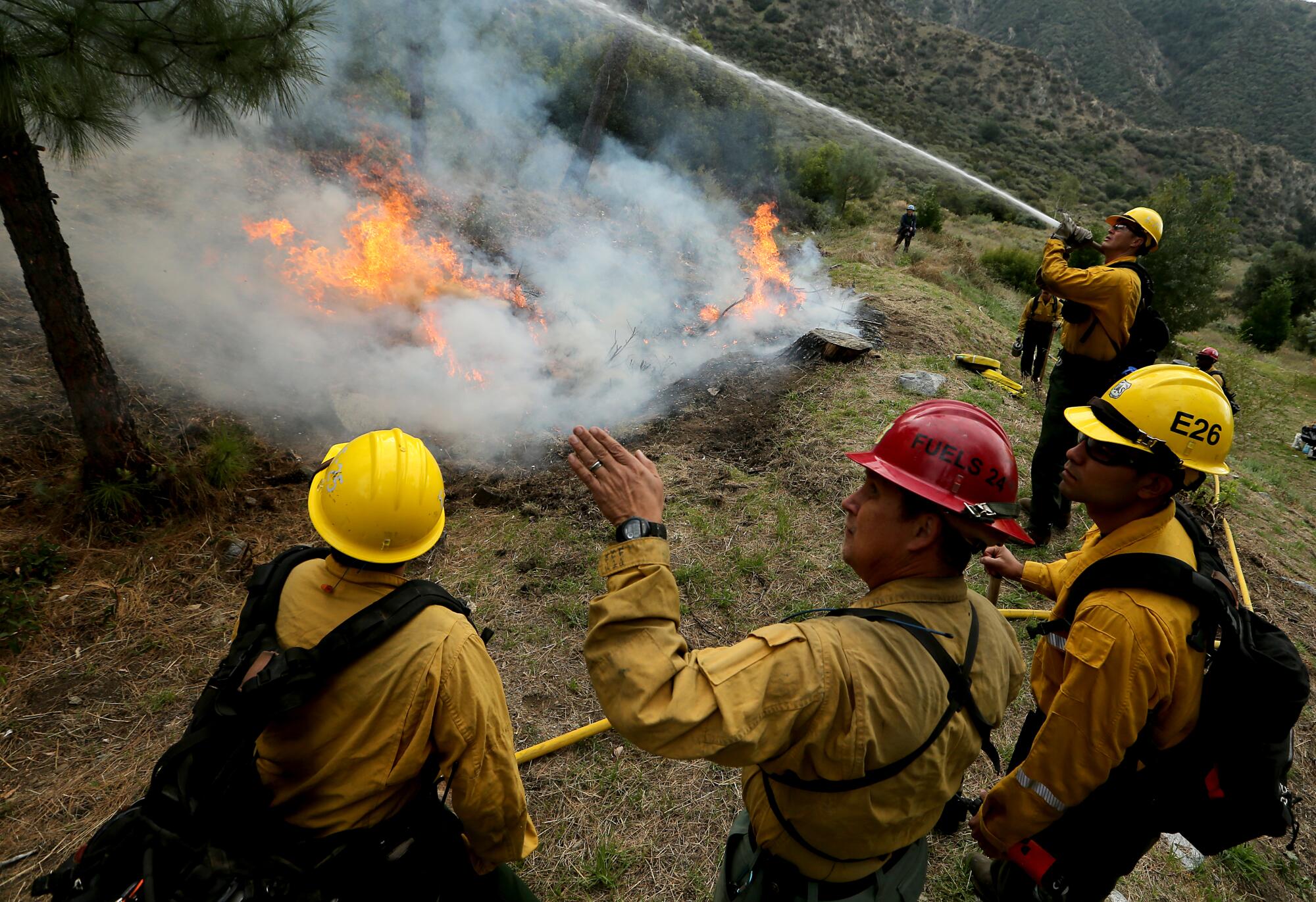 A Forest Service crew member sprays water on vegetation around a prescribed fire