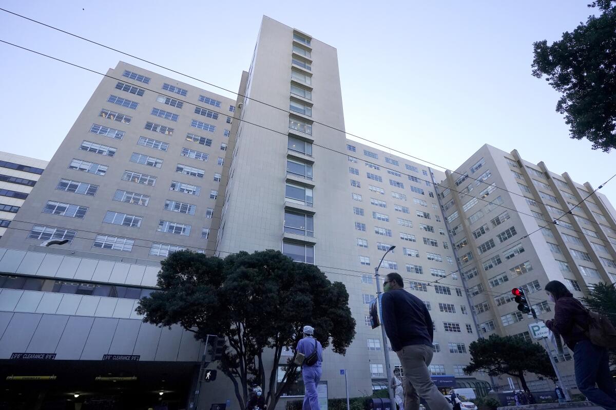 A low-angle view of a person in scrubs and others walking toward the UC San Francisco medical center building