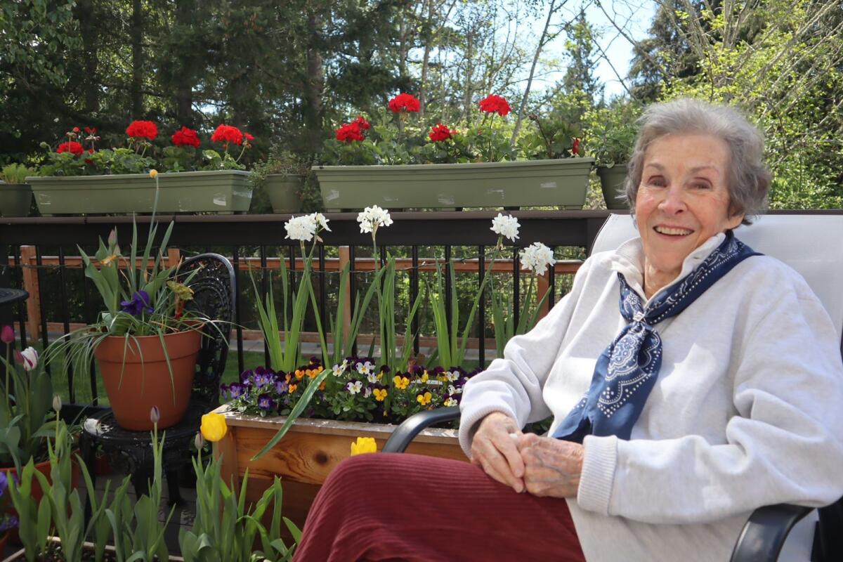 A woman sits on an outdoor patio next to colorful flowers.