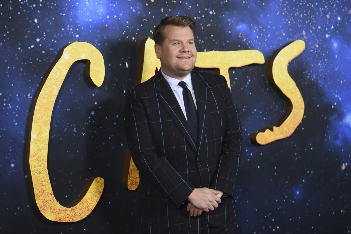 An actor in suit and tie stands and smiles in front of a 'Cats' movie backdrop 