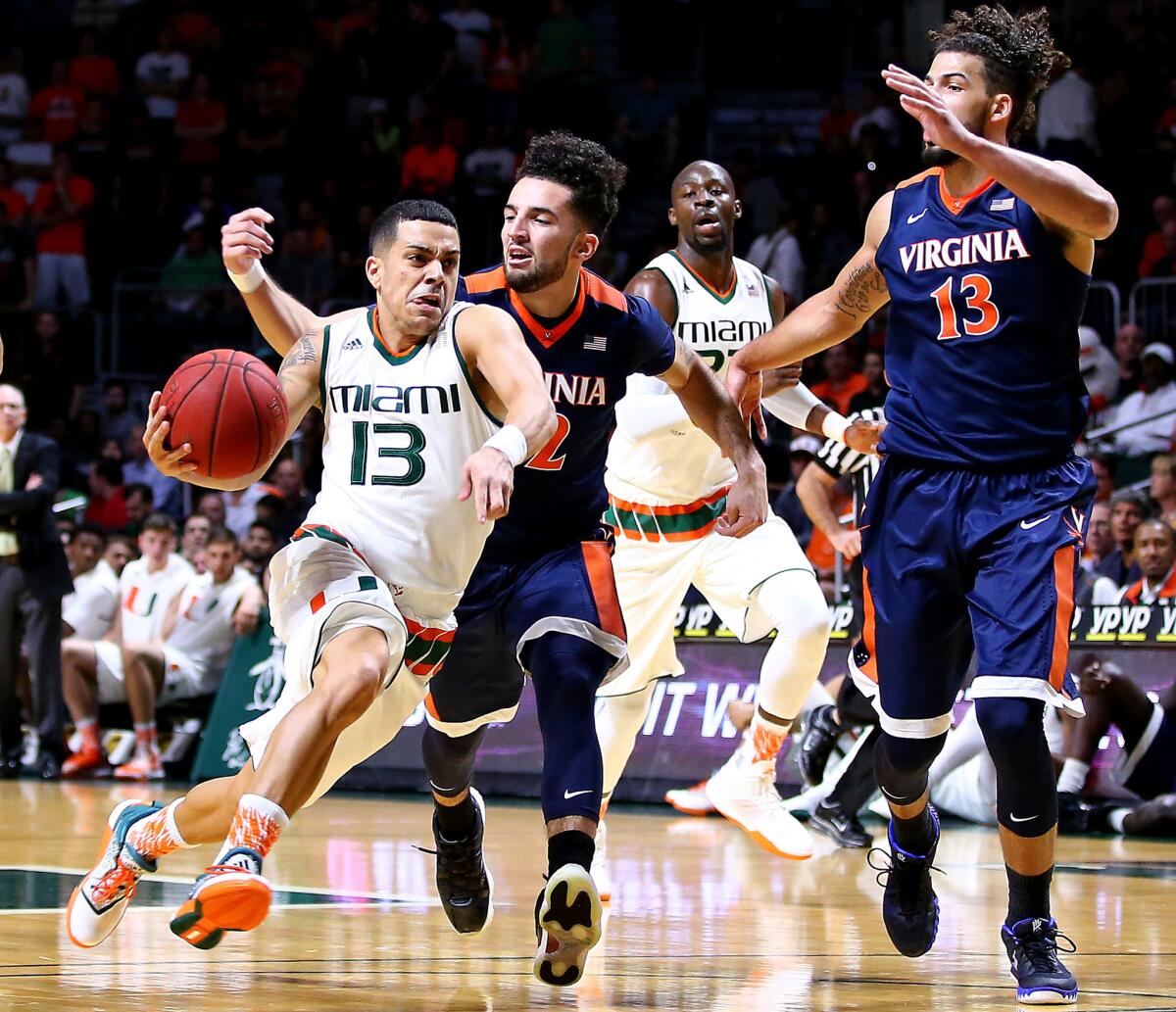 Miami guard Angel Rodriguez (13) drives to the basket while being defended by Virginia's London Perrantes (32) and Anthony Gill (13).