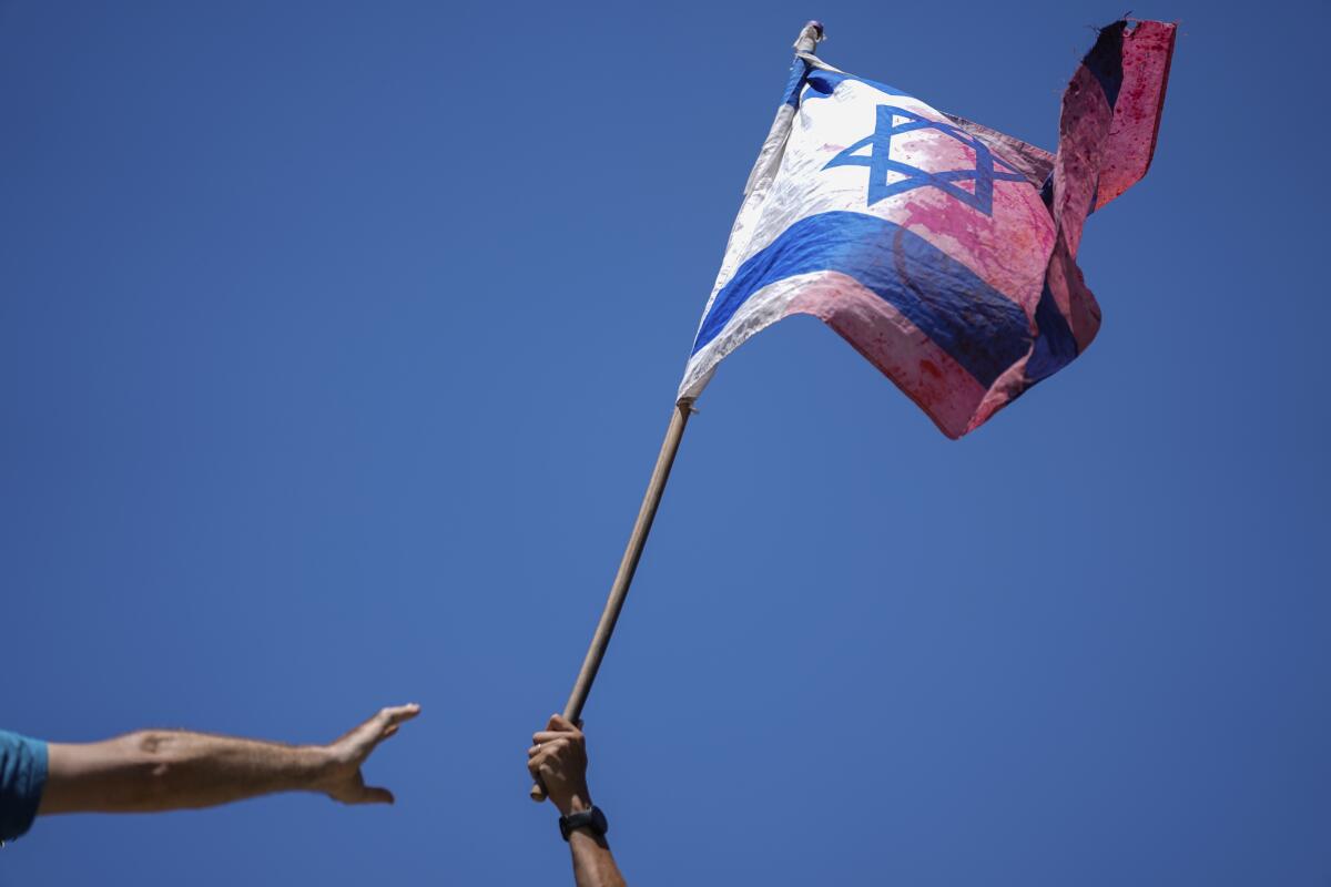 A demonstrator waves an Israeli flag smudged with red coloring during a protest.