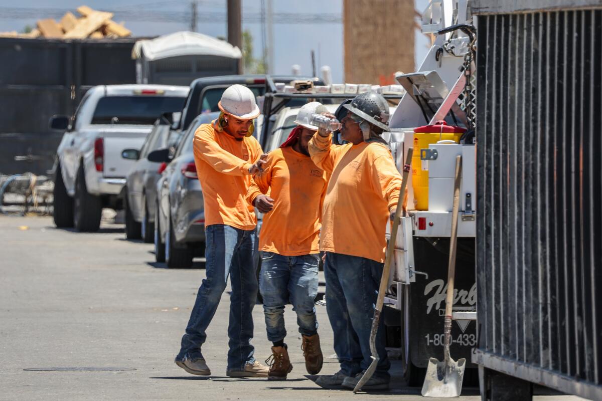 People in orange long-sleeve T-shirts and safety helmets stand in a lot.