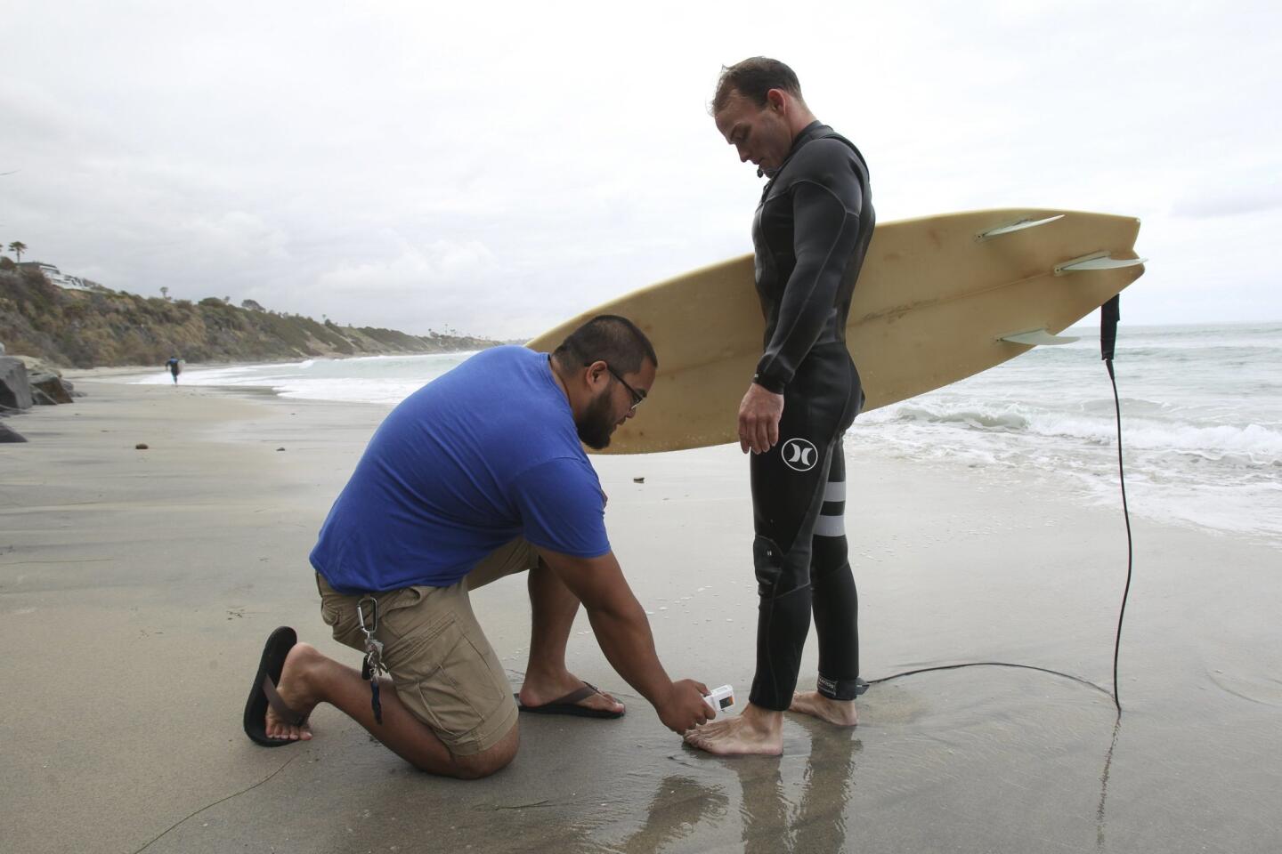 Kinesiology student Alvin Padilla, 24, takes a temperature reading of surfer James Petracca's foot, who volunteered to participate in a wetsuit study by Cal State University San Marcos students, just after he got out of the water.