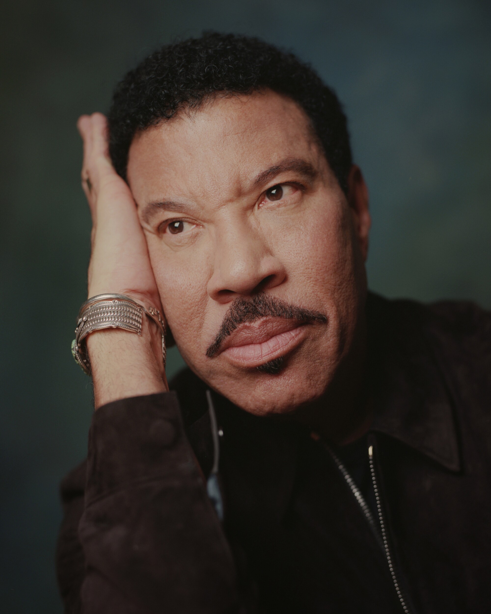 Lionel Richie poses, resting his head against his palm, looking pensive
