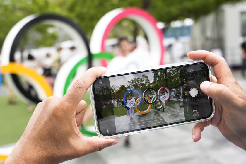 A person takes photos with a mobile device of the Olympic rings outside the Olympic Stadium at the eve of the end of the 2020 Summer Olympics, Saturday, Aug. 7, 2021, in Tokyo, Japan. The Tokyo 2020 Summer Olympics take place in the city from July 23 until Aug. 8, 2021. (AP Photo/Markus Schreiber)