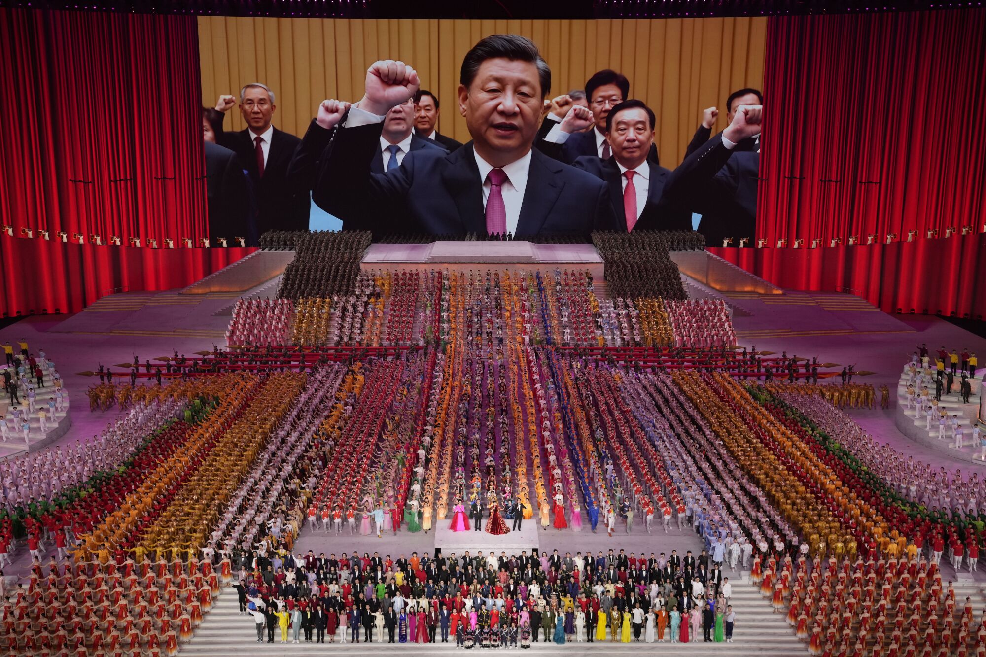 A huge screen shows a group of men in suit and tie raising their fists, the backdrop to a mass assembly of people in a hall