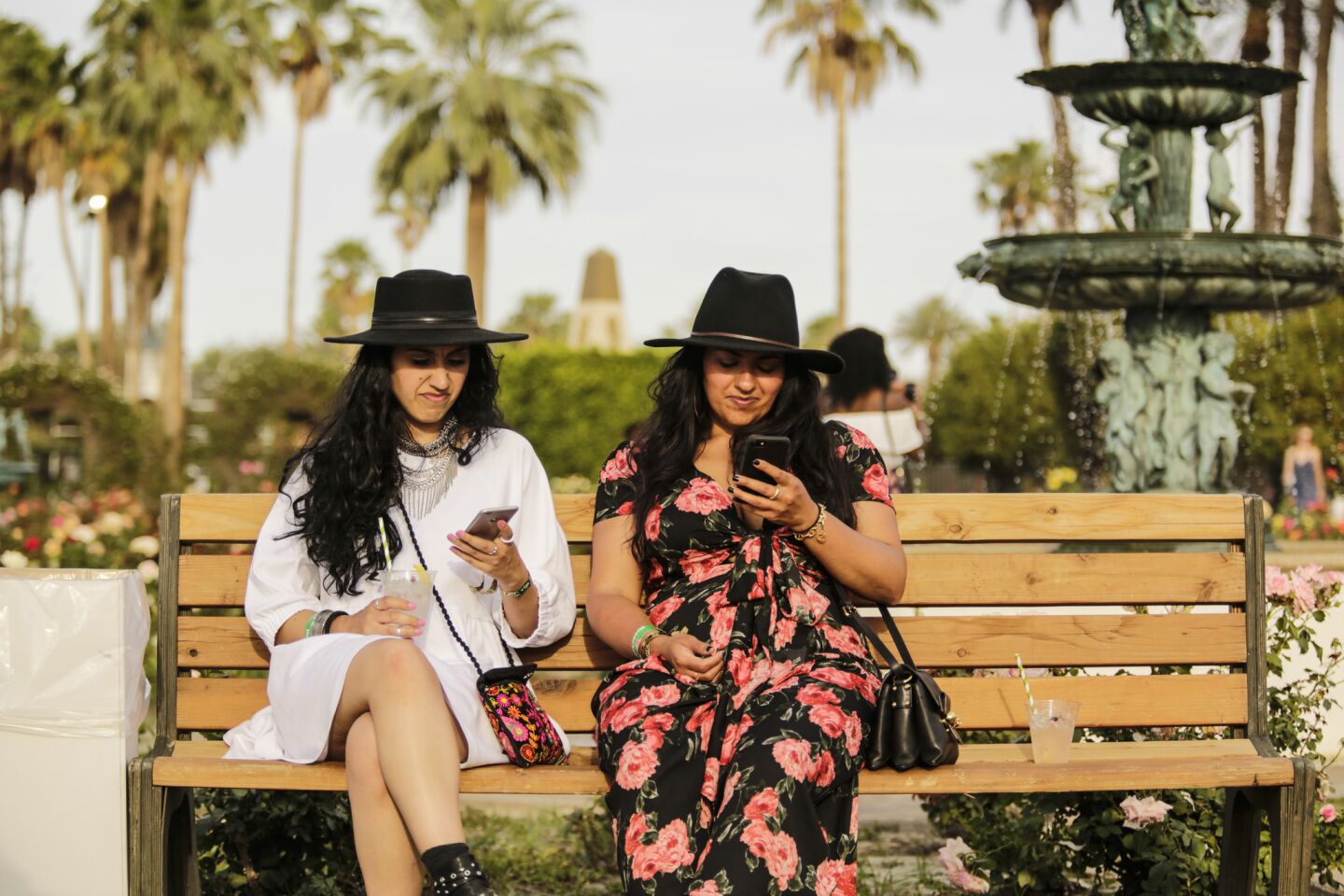 Two women browse their cellphones in the Rose Garden at Coachella.