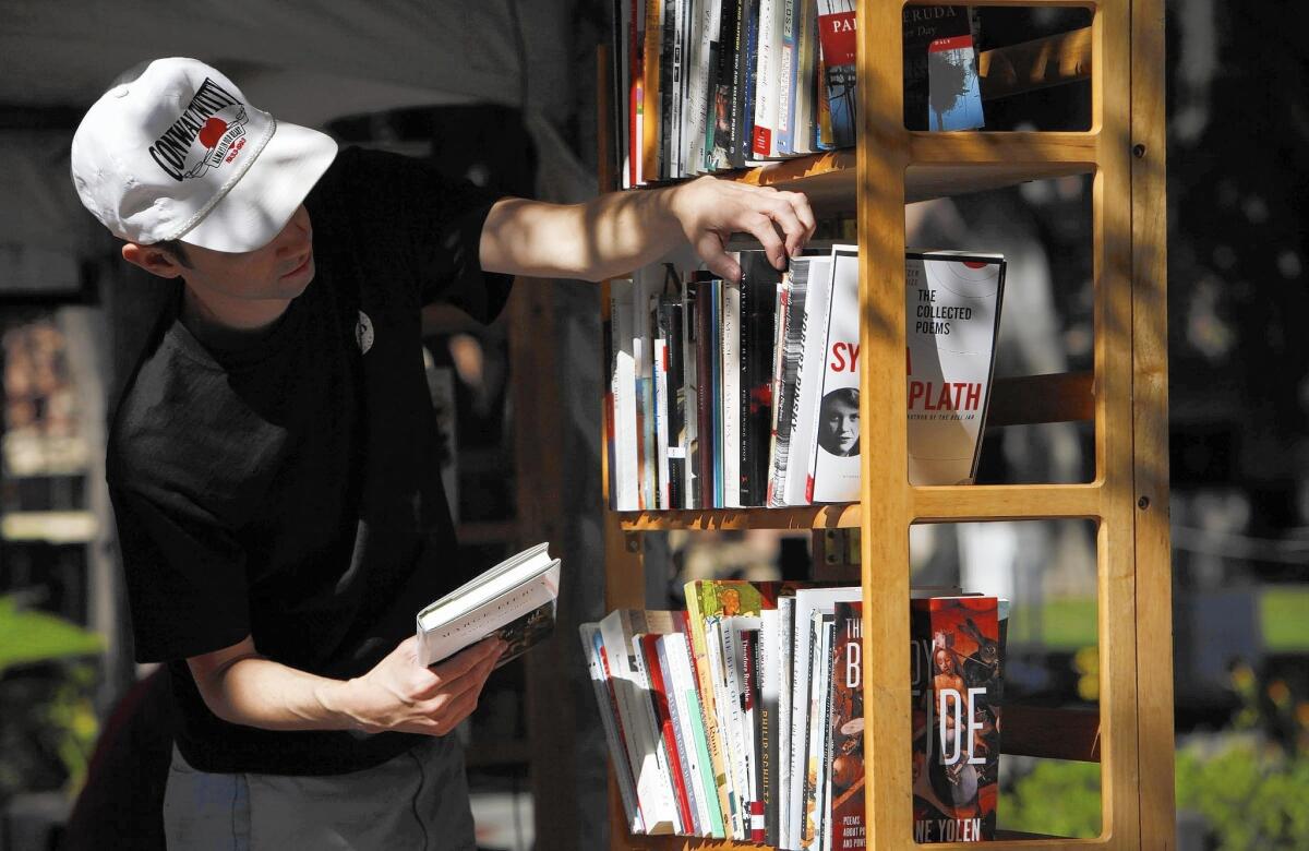 Adam Lipman stocks the bookshelves at the Small World Books and WW Norton booth at the Los Angeles Times Festival of Books, on the USC campus.