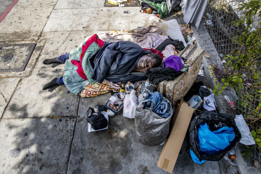 LOS ANGELES, CA - JUNE 2, 2022: Surrounded by her possessions, Jaimie Hope, 35, sleeps on the sidewalk near a bus stop on Western Avenue only blocks away from where Rep. Karen Bass and U.S. Housing and Urban Development Secretary Marcia Fudge visited the EC Motel, which has received federal funding to house the homeless on June 2, 2022 in Los Angeles, California. Bass and Fudge toured the city's facilities which received funding for the homeless crisis. Hope has been living on the streets for the past two years.(Gina Ferazzi / Los Angeles Times)
