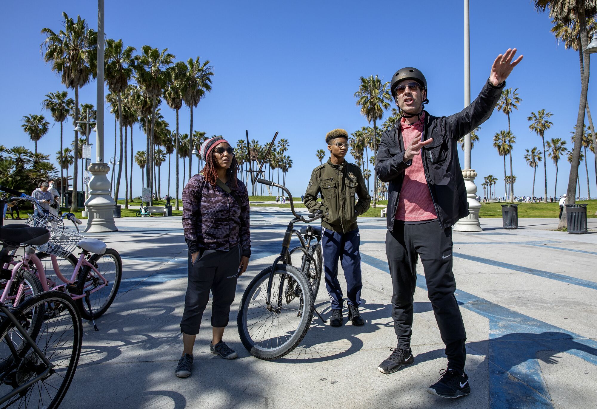 A man, right, stops by Venice Beach while giving a tour to a woman and her son.