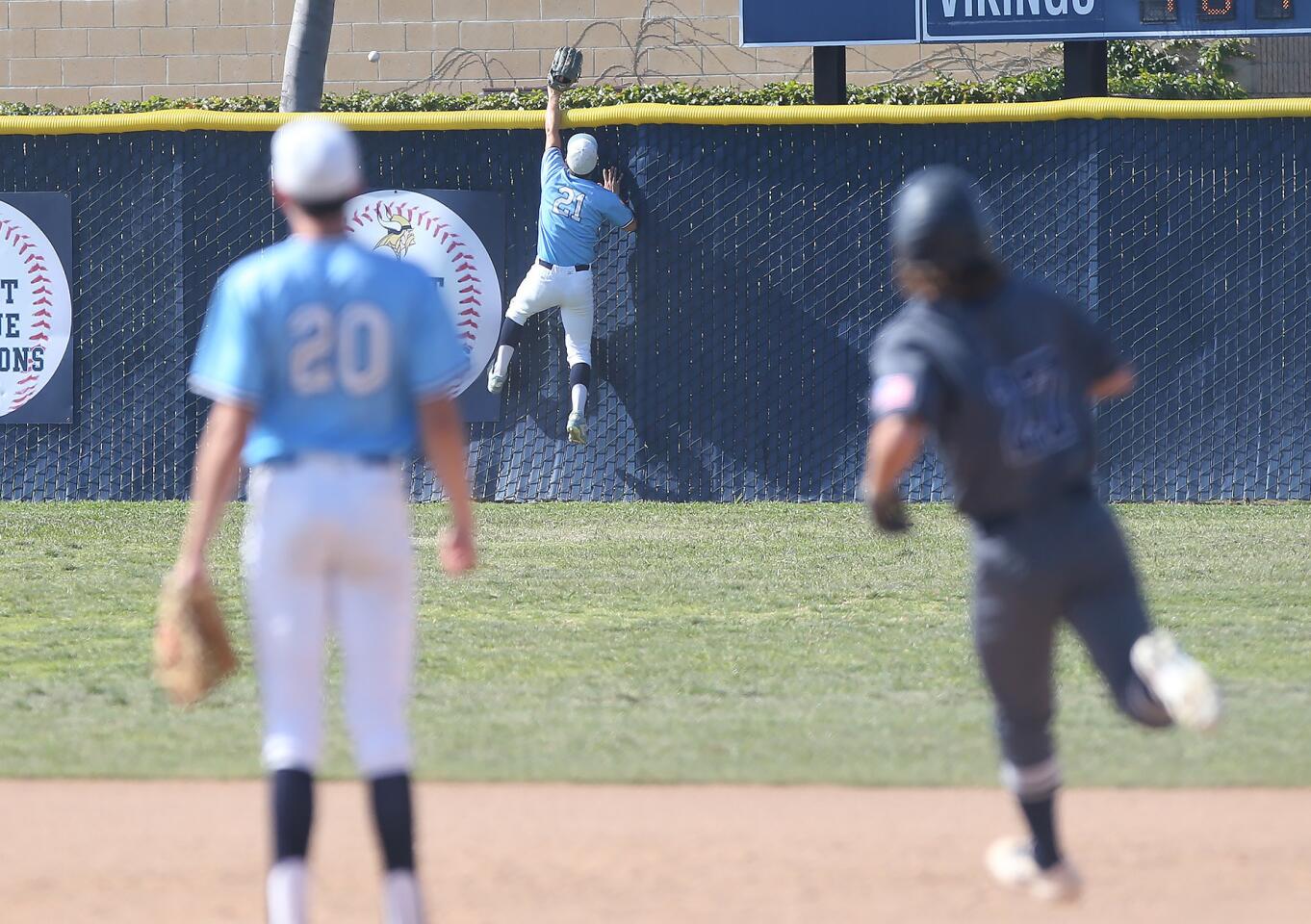 Newport Harbor's Jack Bibb, right, watches the ball sail over the right-field fence as Marina's Austin Hallman (21) tries to climb the fence to catch it during a Wave League game on Tuesday.